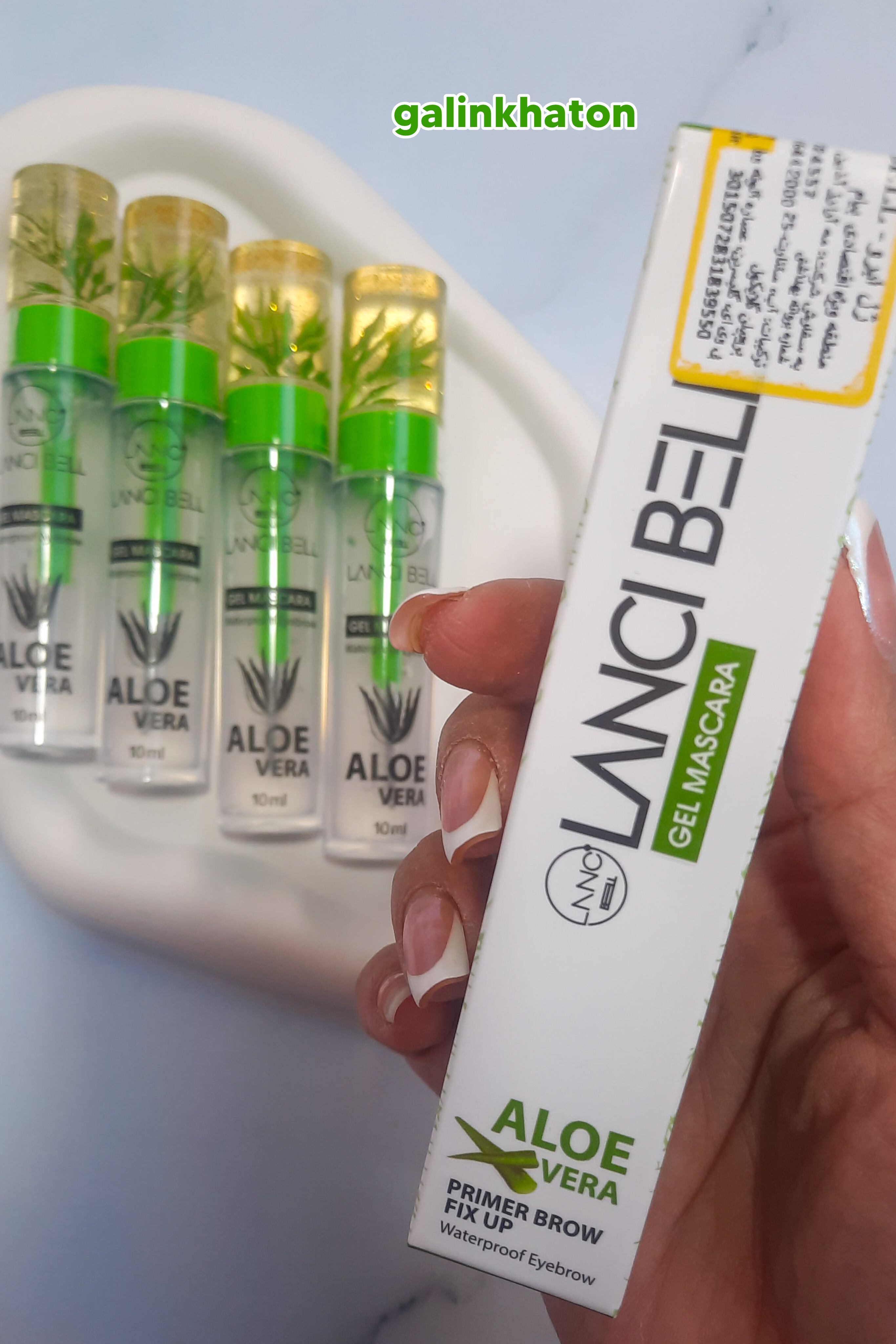 «چهار ژل ابرو لنسیبل روی شیپ سنگی سفید، جعبه در دست، نمایش شیک برند و بسته‌بندی جذاب محصول آرایشی.»