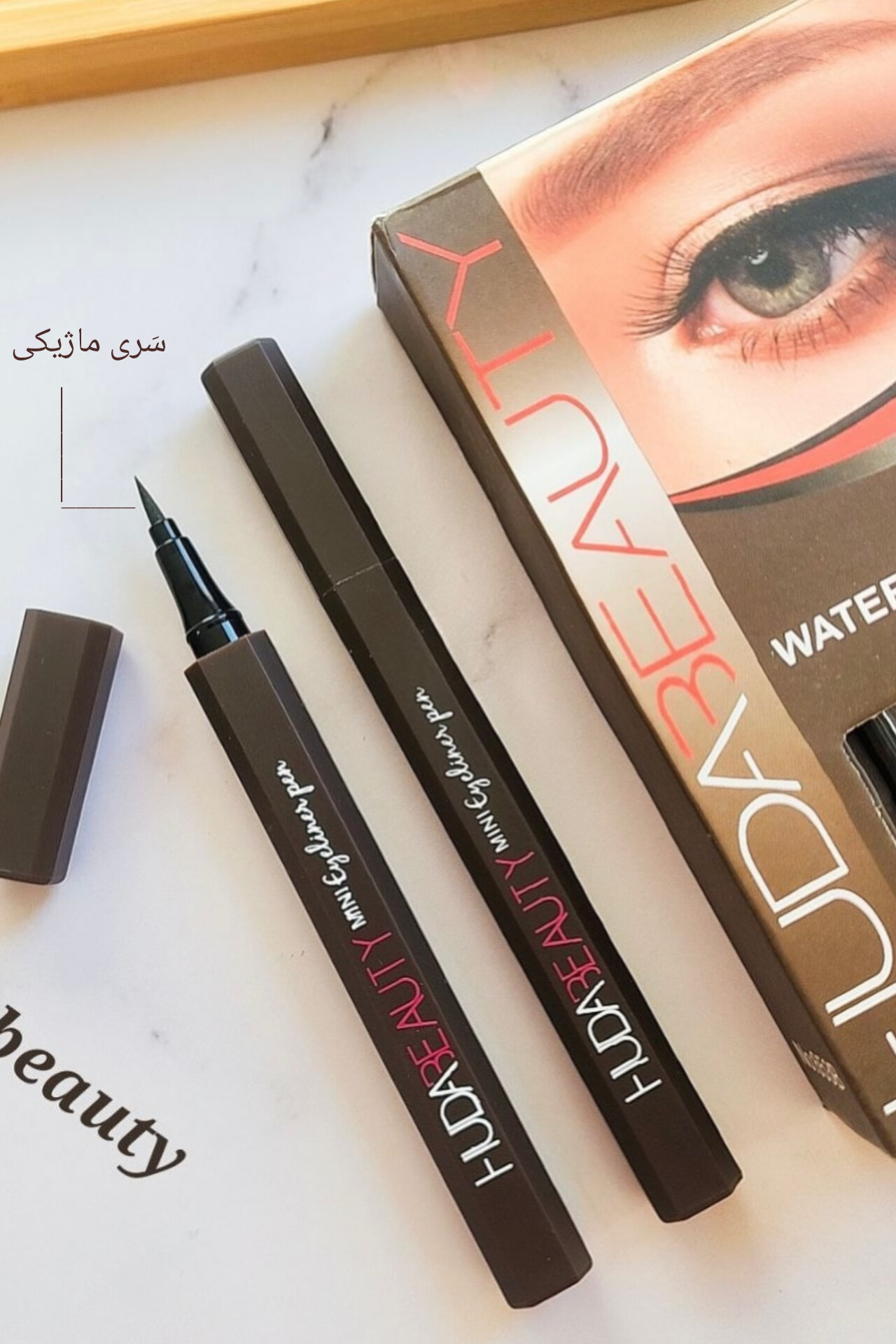 «دو خط چشم ماژیکی قهوه‌ای HUDA BEAUTY کنار هم، یکی باز با قسمت ماژیکی مشخص، ایده‌آل برای کشیدن خطوط دقیق و جذاب چشم.»