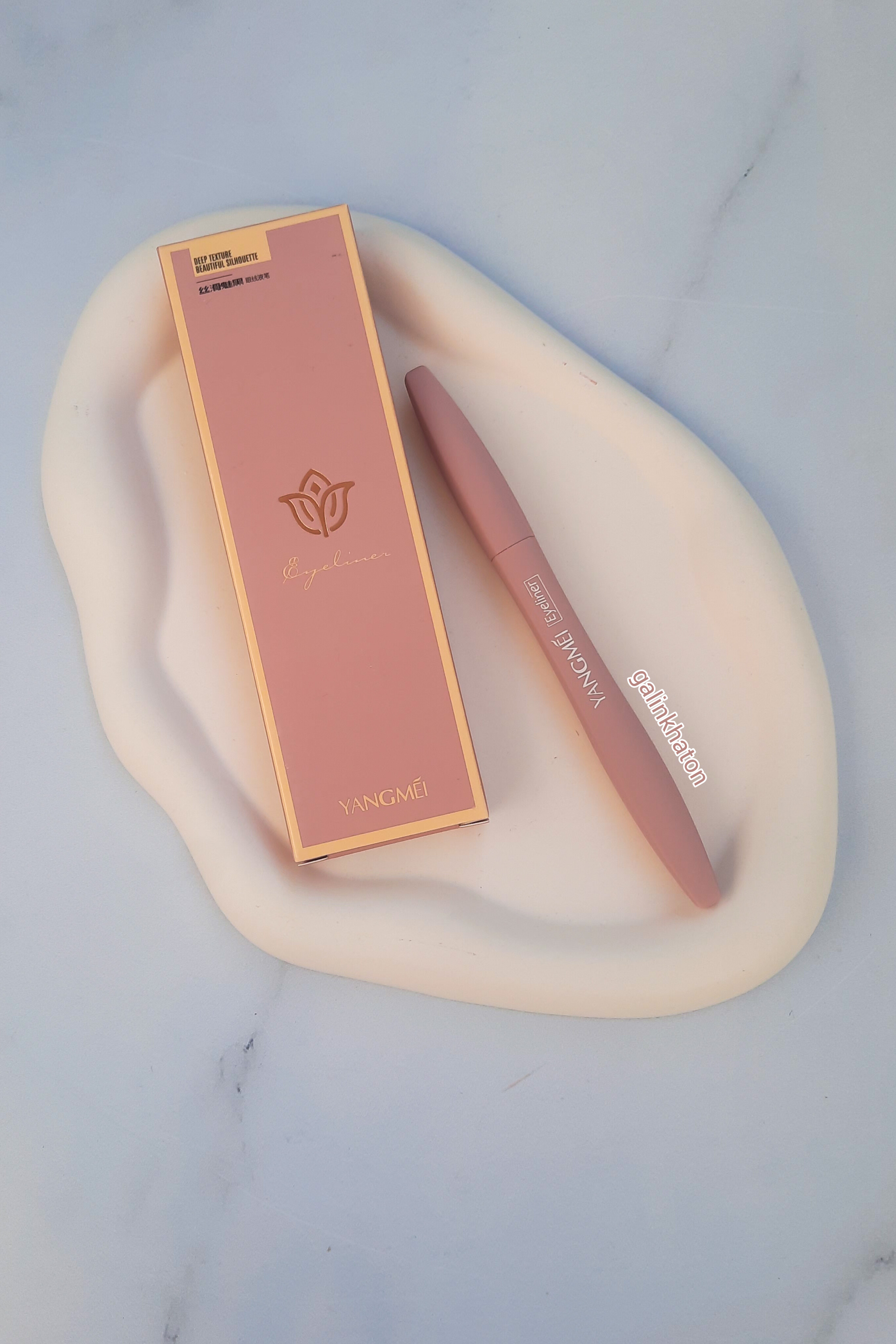 خط چشم ماژیکی یانگمی مشکی کنار جعبه روی شیپ سنگی سفید دفرمه، نمای نزدیک محصول، ضد آب و مات