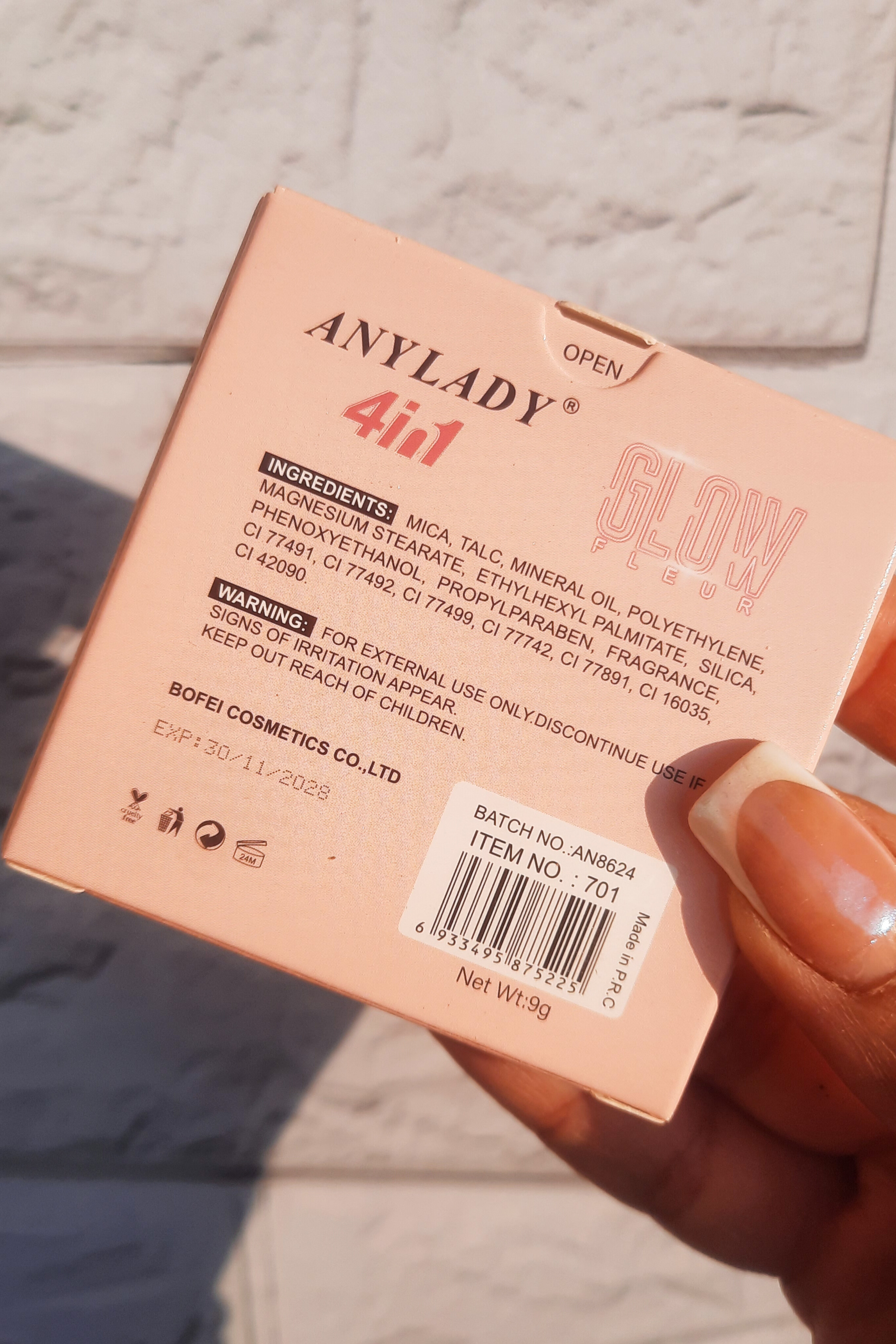 جعبه هایلایتر و رژگونه آنیلیدی در دست، نمای نزدیک پشت جعبه، جزئیات بسته‌بندی و برند مشخص