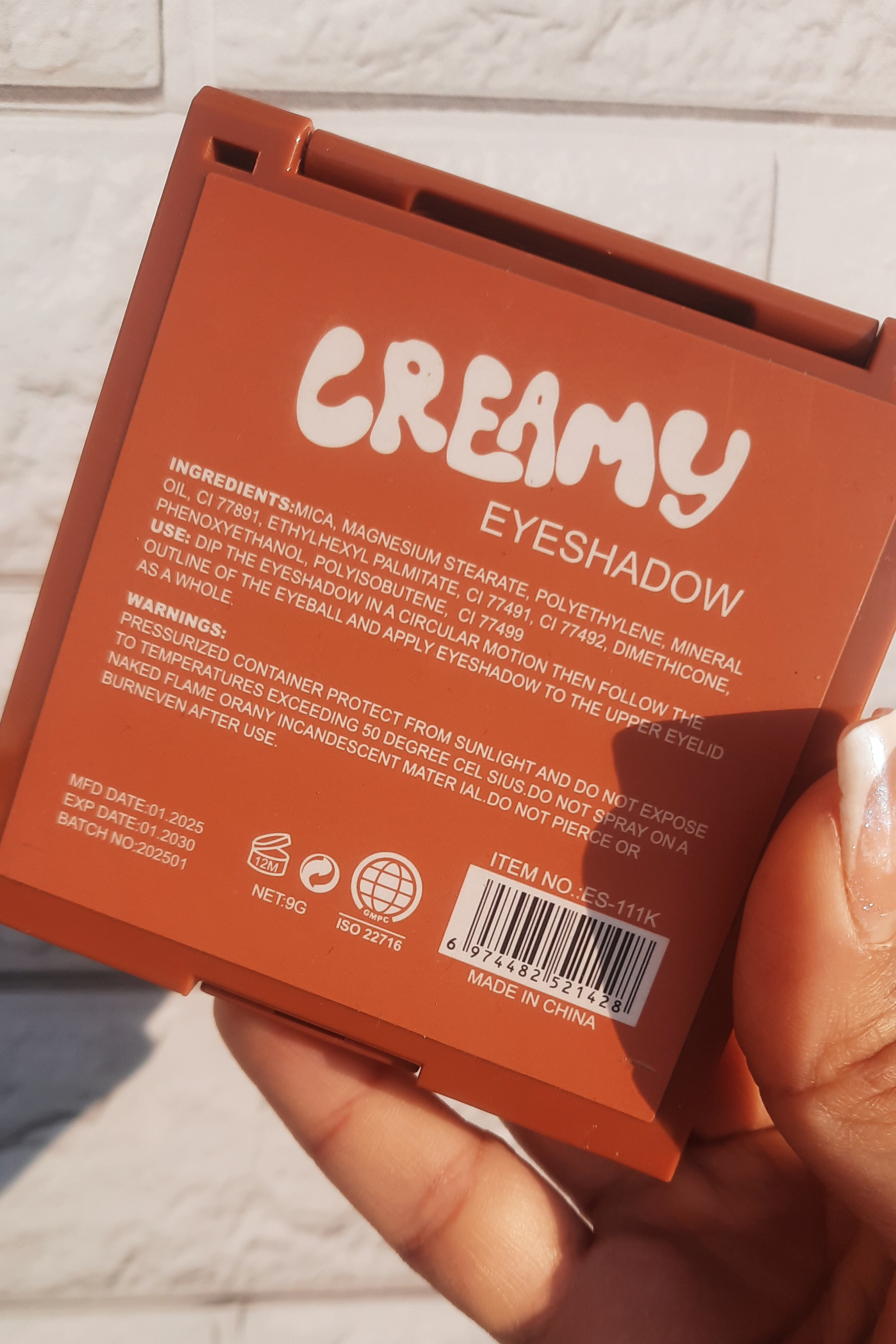 پالت سایه ۹ رنگ کرمی هدی موجی در دست؛ نمای نزدیک پشت محصول و اطلاعات درج‌شده برای بررسی کیفیت